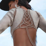 A woman stands outdoors with her back to the camera, wearing AYA Sacred Wear’s Cotton Maxi Dress in Light Sage—a long sleeve, backless, flowing bohemian silhouette—capturing an effortlessly chic style.