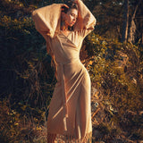 Amidst lush greenery and rocks, a person exudes confidence in an earthy-toned Boho Maxi Skirt from AYA Sacred Wear. Crafted from sustainable cotton, this eco-conscious piece features dramatic flair and a tasseled hem, all bathed in the warm glow of sunlight.