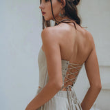 A woman with long braided hair elegantly wears the Boho Top Corset and Skirt Women in a sage green shade, a summer crop top and skirt set from AYA Sacred Wear. The lace-up back corset design of the dress offers a unique blend of style and sustainability, creating an eye-catching contrast against the plain background.