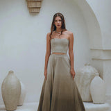 A woman poses gracefully in the Boho Top Corset and Skirt by AYA Sacred Wear, showcasing the sage green summer crop top and skirt set against a minimalist backdrop featuring white textured vases and a curved arch, creating a soft, elegant atmosphere.