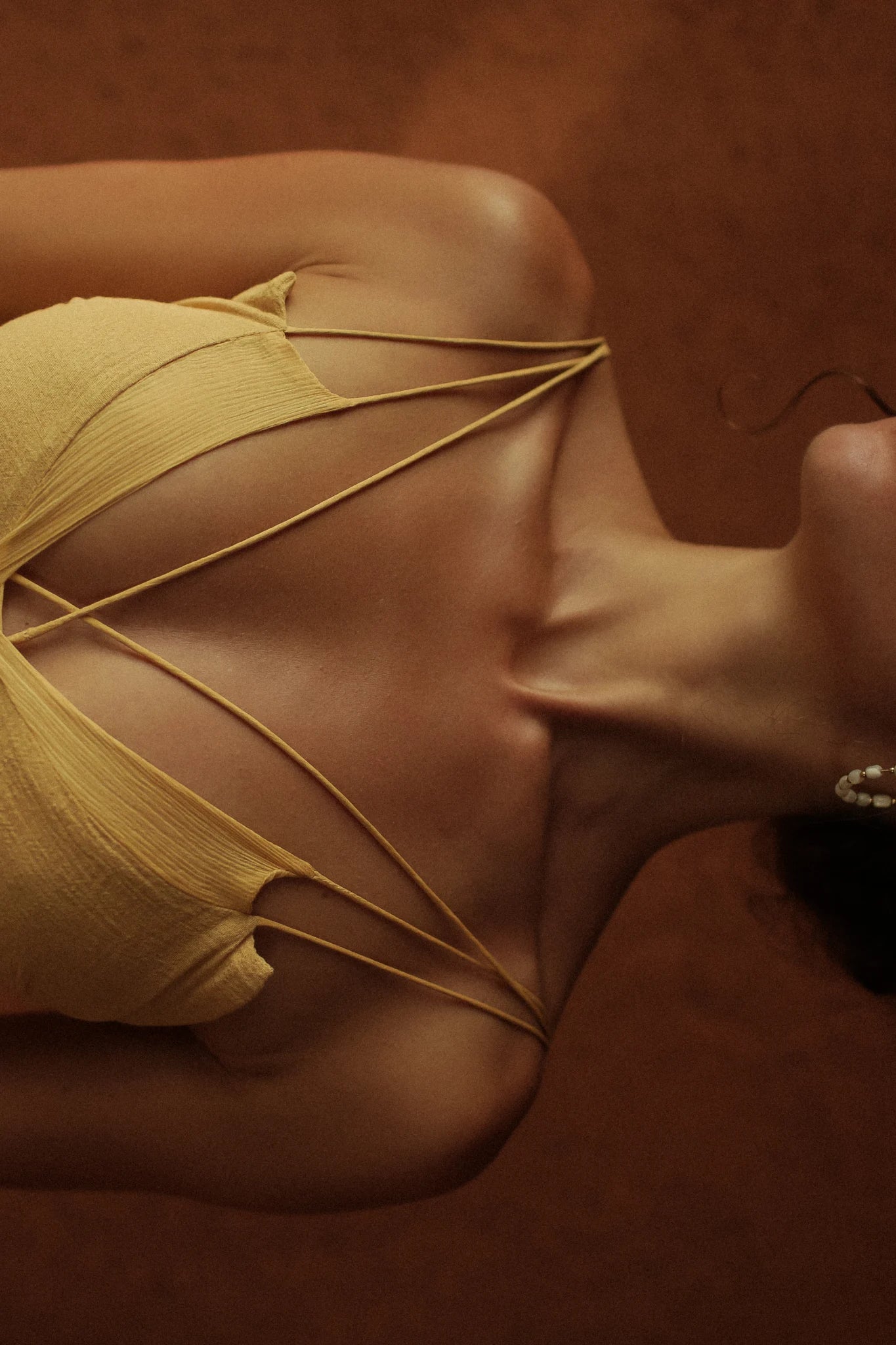 A person wears the AYA Sacred Wear Powder Yellow Padma Dress, shown from the shoulders up with their collarbone and neck visible against a brown background.