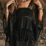 A person wearing a dark, fringed poncho over an AYA Sacred Wear Hand Loomed Cotton Blouse, beautifully paired with bold jewelry like rings, bracelets, and a necklace. They stand outdoors against a rugged rock background, with tousled hair and dark lipstick.
