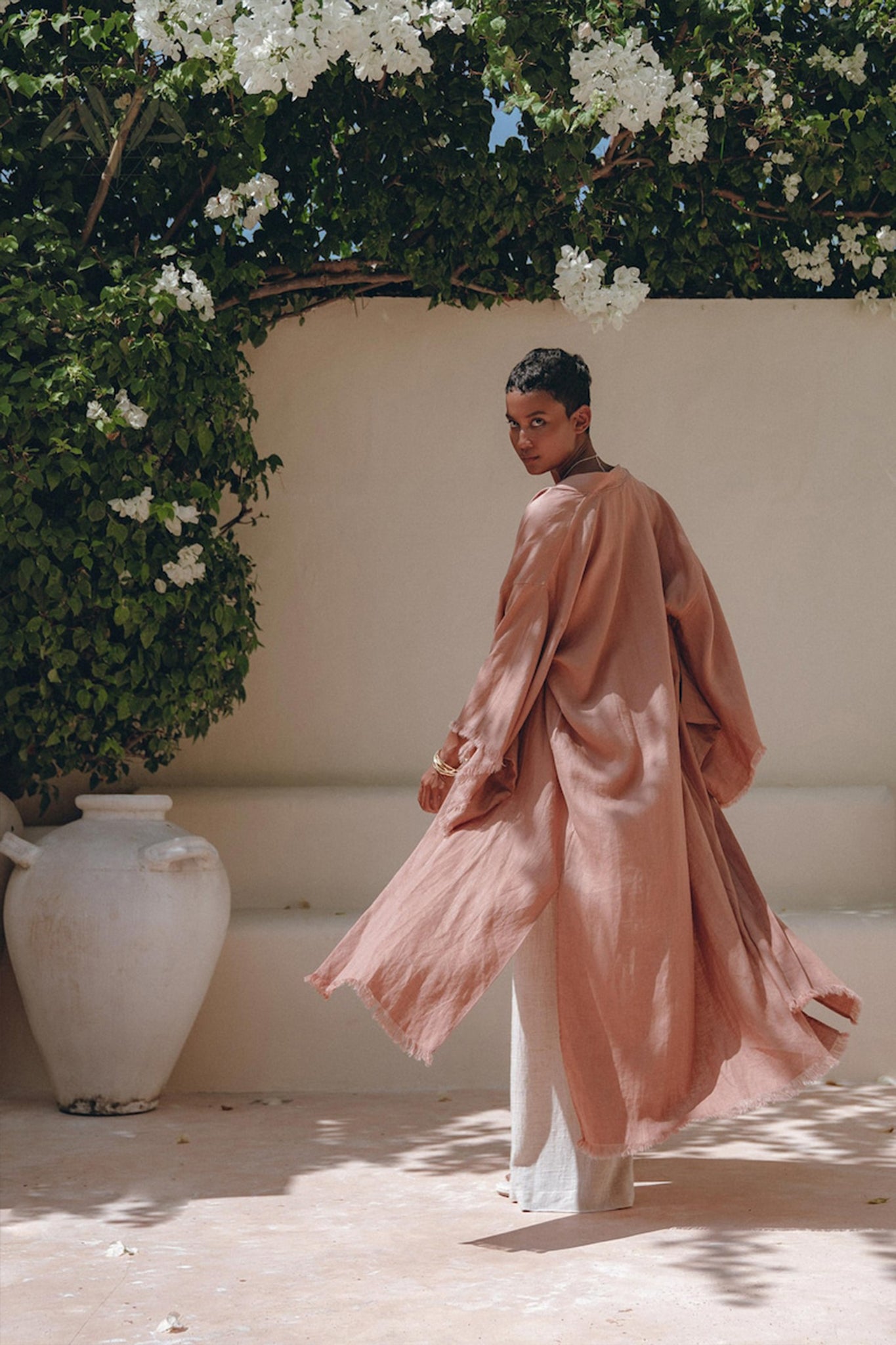 A woman wearing the AYA Sacred Wear's Linen Cardigan Women in dusty pink radiates effortless elegance, seamlessly blending bohemian charm with the gentle touch of organic linen.