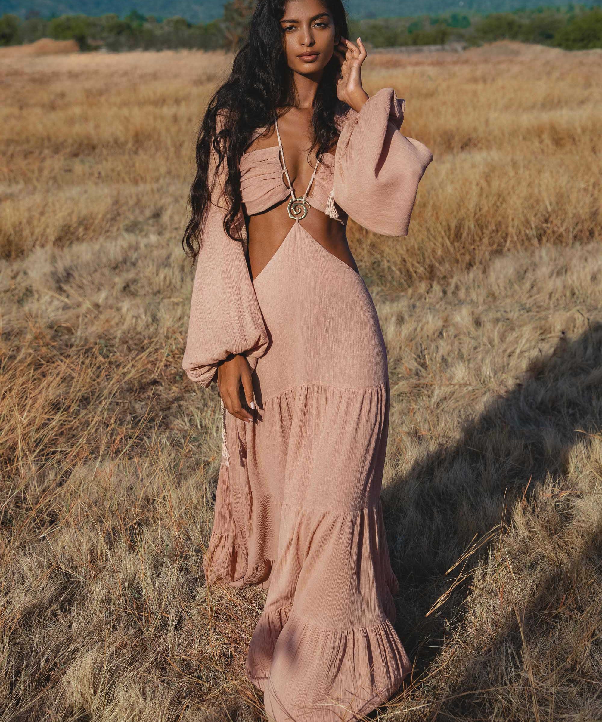 Woman in a pink dress standing in a field with mountains in the background