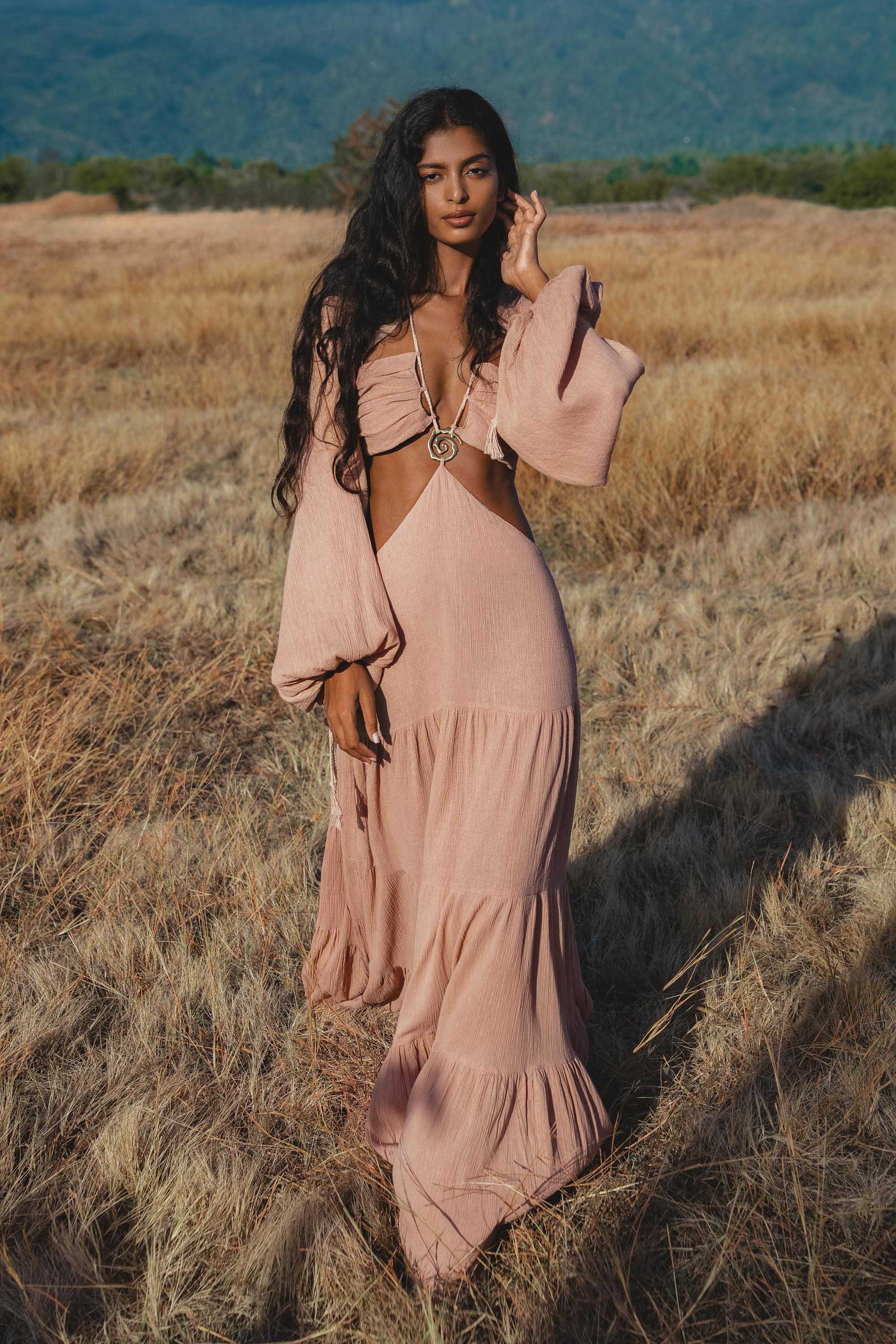 Woman in a pink dress standing in a field with mountains in the background