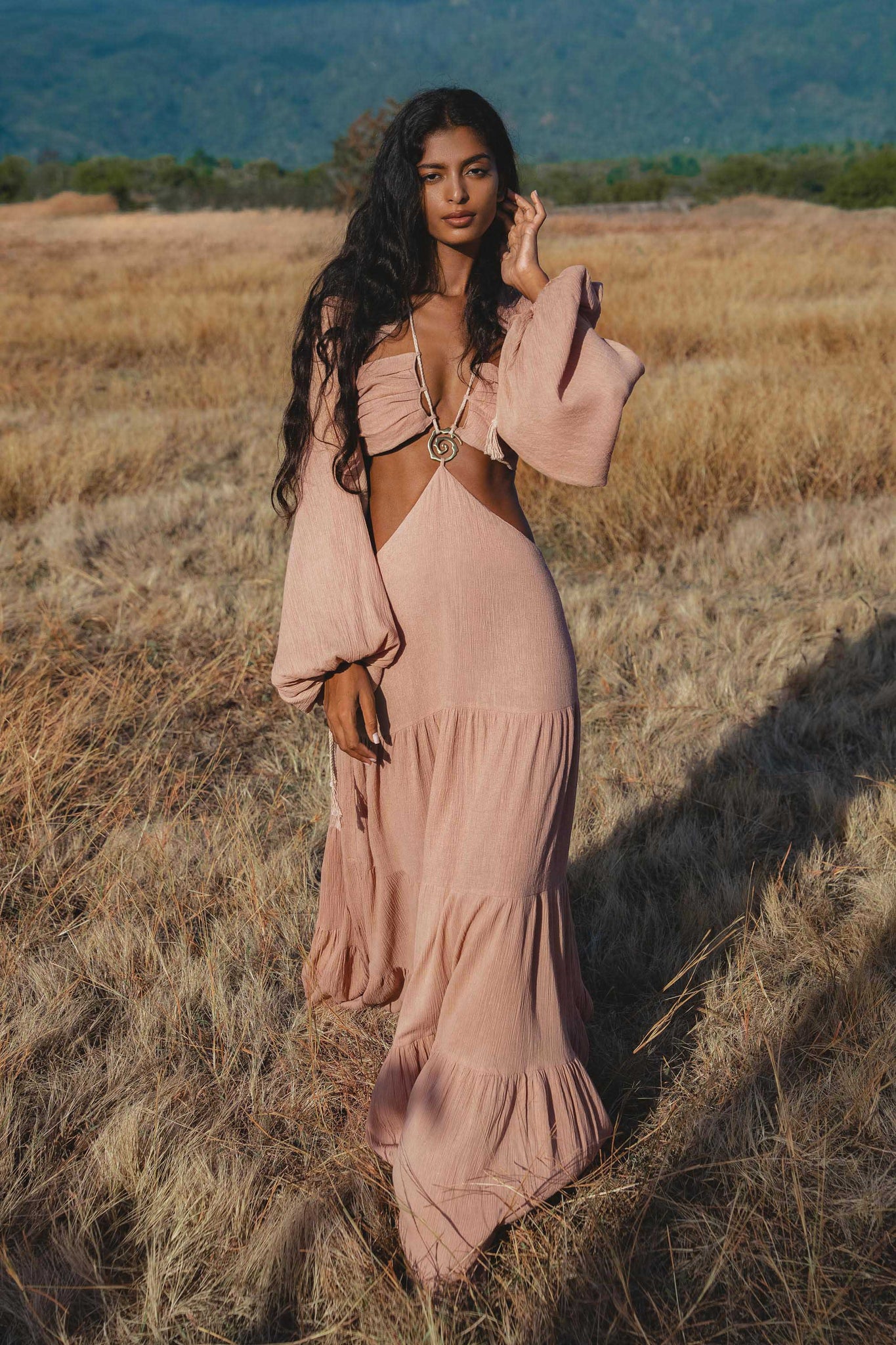 Woman in a pink dress standing in a field with mountains in the background