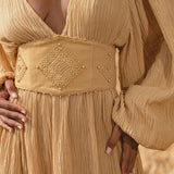 A woman wears the Tatva Dress in Saffron Gold Colour by AYA Sacred Wear, botanically dyed and paired with a handcrafted belt.