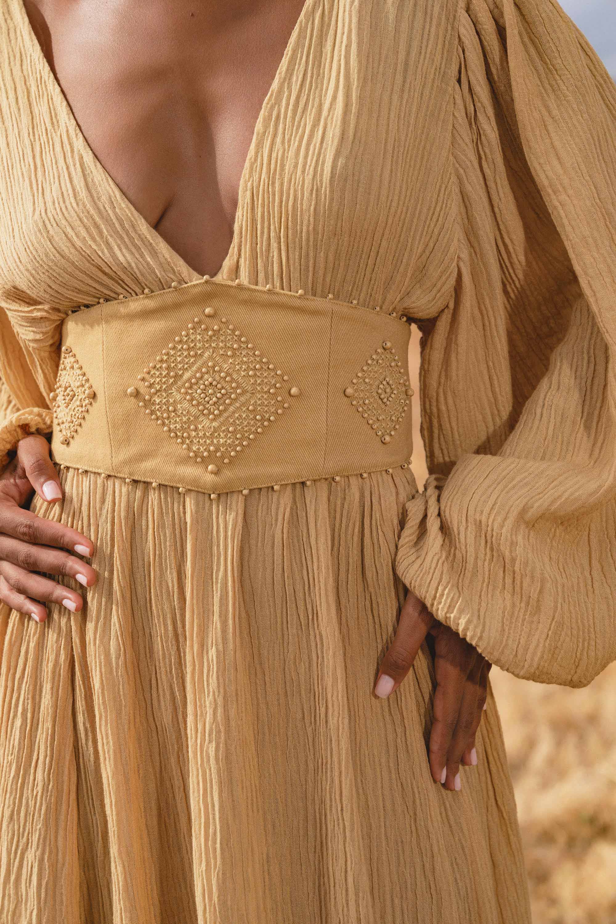 A woman wears the Tatva Dress in Saffron Gold Colour by AYA Sacred Wear, botanically dyed and paired with a handcrafted belt.