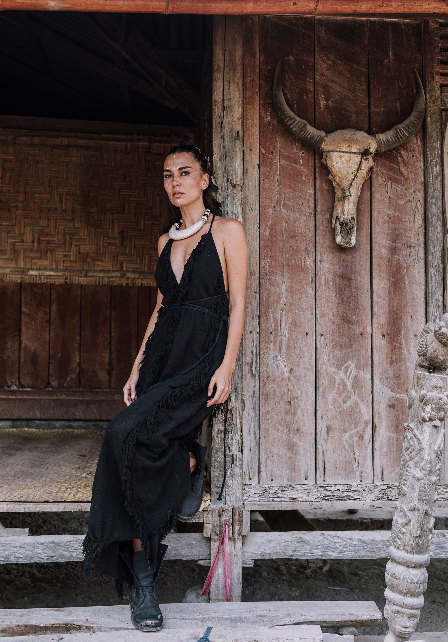 A model wearing the timeless Black raw cotton goddess dress by AYA Sacred Wear, standing gracefully on the wooden steps of a rustic cabin.