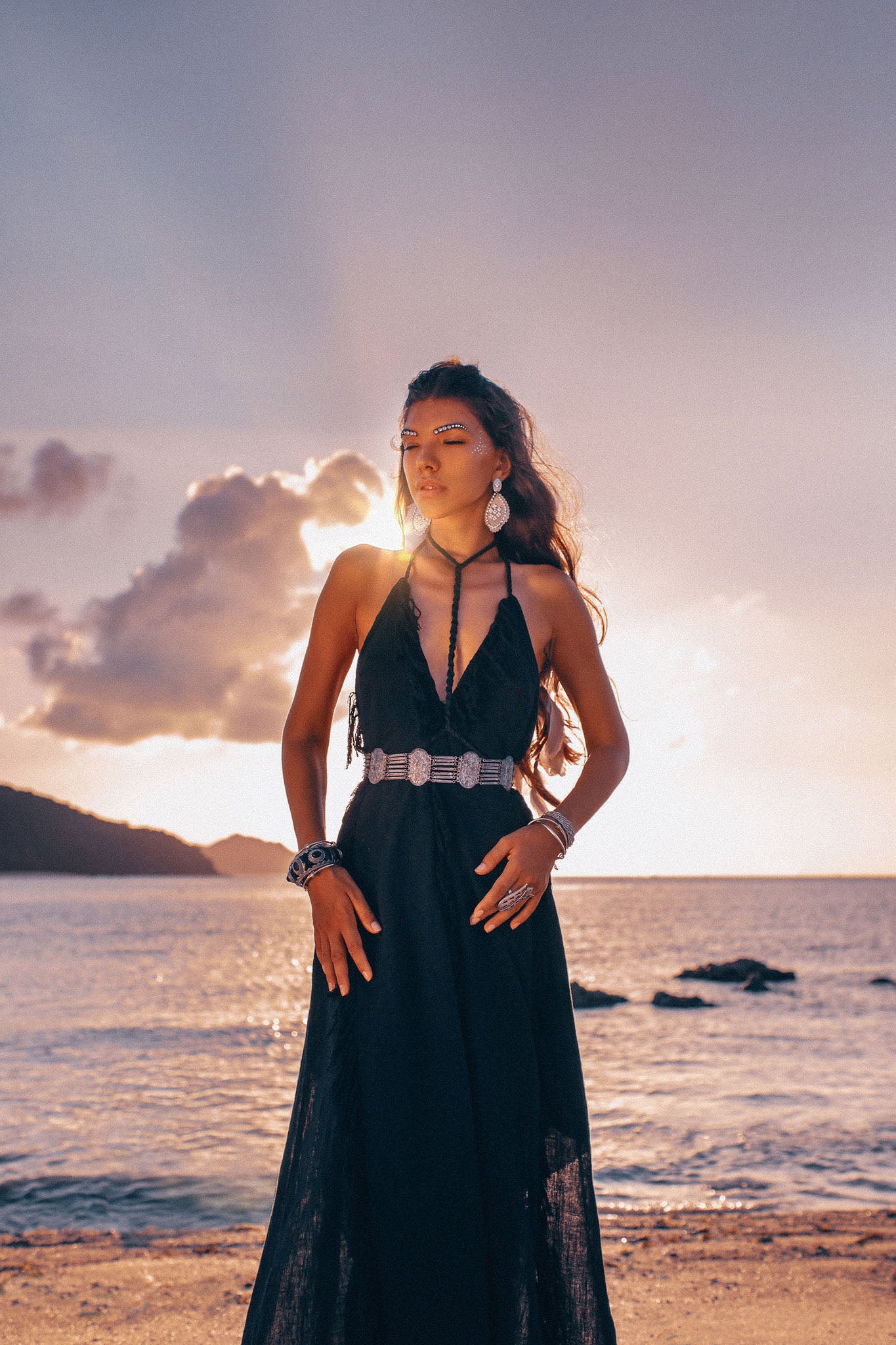 Full-length shot of a model standing on a beach at sunset, showcasing the flowy drape of the Black organic cotton fringe dress.