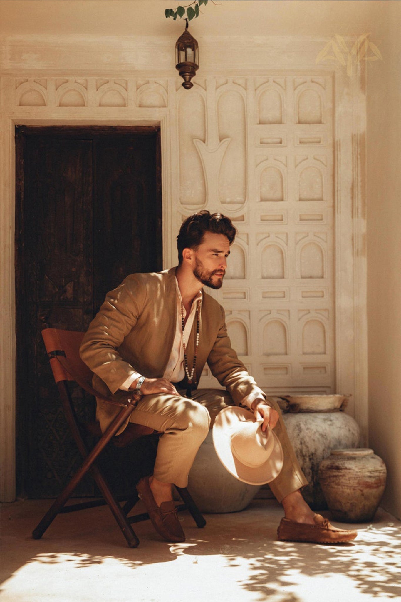 Side view of a man sitting on a wooden folding chair in an earthy brown botanically dyed linen suit jacket.