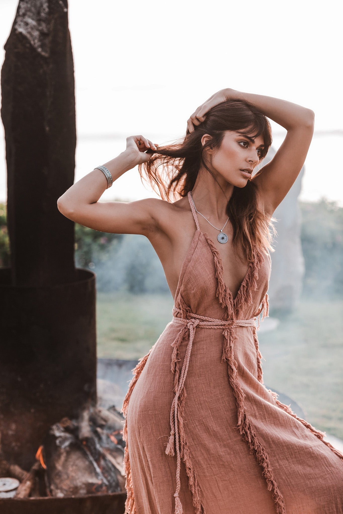 Outdoor portrait of a model posing in the Dusty Rose deep V-neck dress against a dark volcanic stone background.