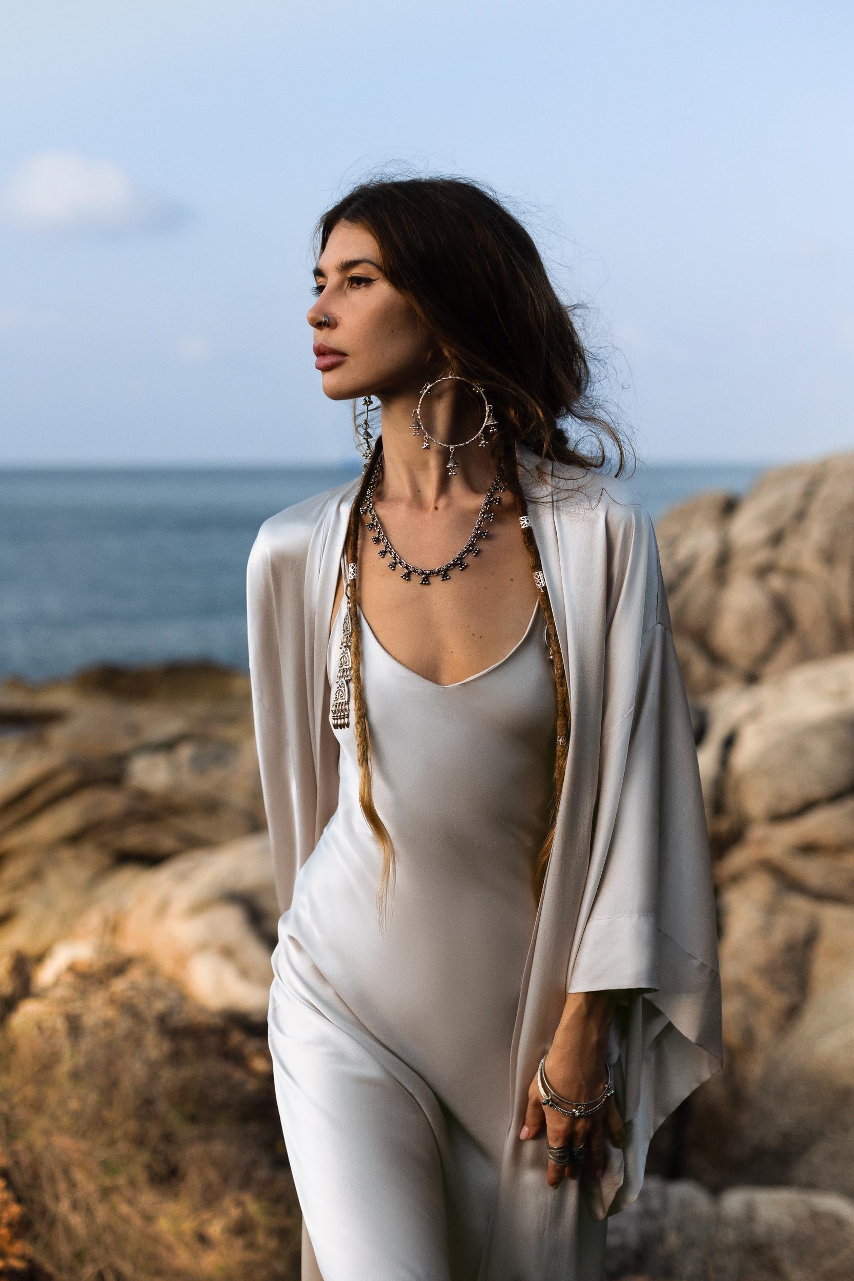 Indulge in the timeless elegance of the Silk Kimono in Mist Blue, a luxurious floor-length robe that combines both style and comfort. Crafted from premium silk, this kimono glides effortlessly over the body, capturing the light with a soft, radiant golden sheen. Its flowing, relaxed silhouette offers an effortlessly chic look, perfect for adding a touch of elegance to any outfit.