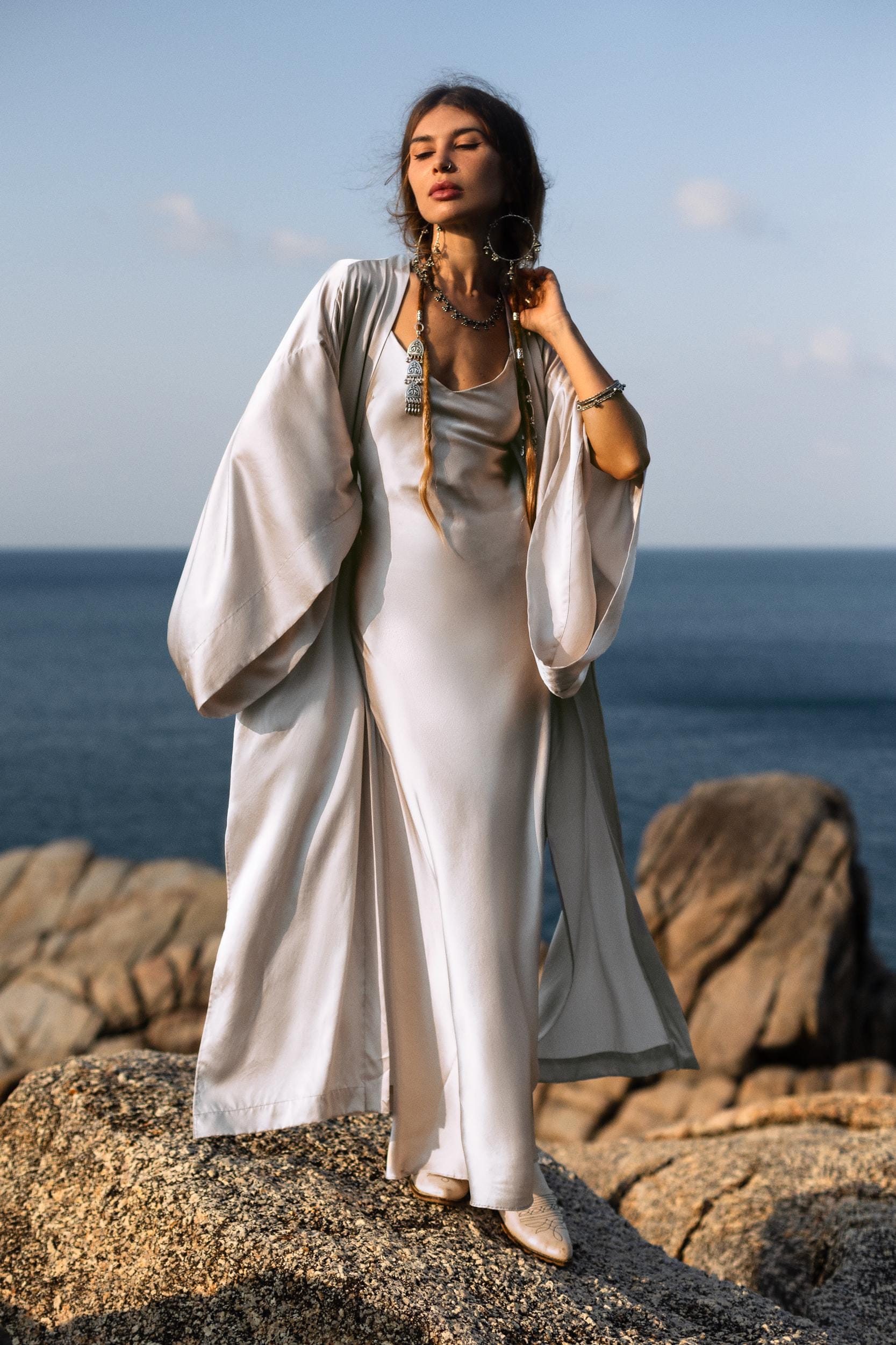 Indulge in the timeless elegance of the Silk Kimono in Mist Blue, a luxurious floor-length robe that combines both style and comfort. Crafted from premium silk, this kimono glides effortlessly over the body, capturing the light with a soft, radiant golden sheen. Its flowing, relaxed silhouette offers an effortlessly chic look, perfect for adding a touch of elegance to any outfit.