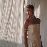A woman in the AYA Sacred Wear Off-White Tribal Goddess Slip Over, an ethnic handwoven macrame sheer net layer-up, stands before cream curtains, gazing to the side as natural light highlights her look.