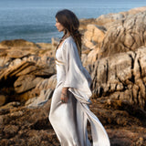 Streamlined silhouette of the open-front Mist Blue silk duster robe during golden hour on Bali coast