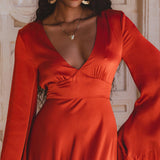A close-up of a model wearing the Peace Silk Maxi Dress in Wine Red. The dress features a deep V-neckline and elegant bell sleeves, showcasing a silky texture that drapes beautifully. The model is accessorized with gold hoop earrings and a delicate necklace, exuding a chic and sophisticated look perfect for a beach wedding.