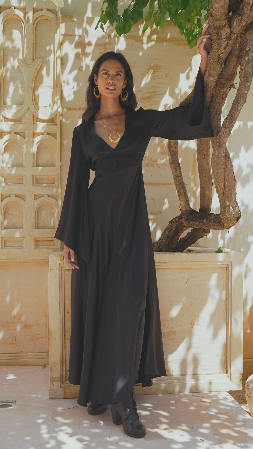Explore the elegance of the Black Gloss Goddess Dress - a bohemian maxi dress with an open back and bell sleeves. Perfect for evening cocktails and formal occasions, crafted with ethically-sourced silk.