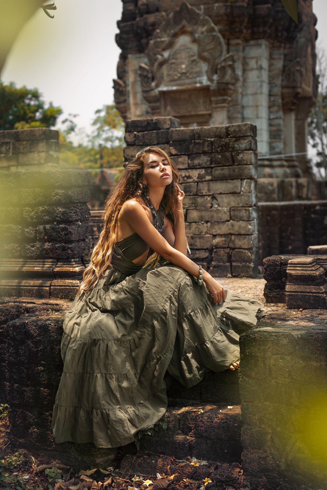 Woman sitting gracefully on ancient stone ruins in a dark green organic cotton goddess maxi dress with a long flowy skirt.