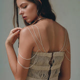 A woman with long brown hair in a braid wears the Sage Green Tribal Goddess Slip Over by AYA Sacred Wear—an ethnic, handwoven macrame sheer net dress—standing sideways and looking down thoughtfully.