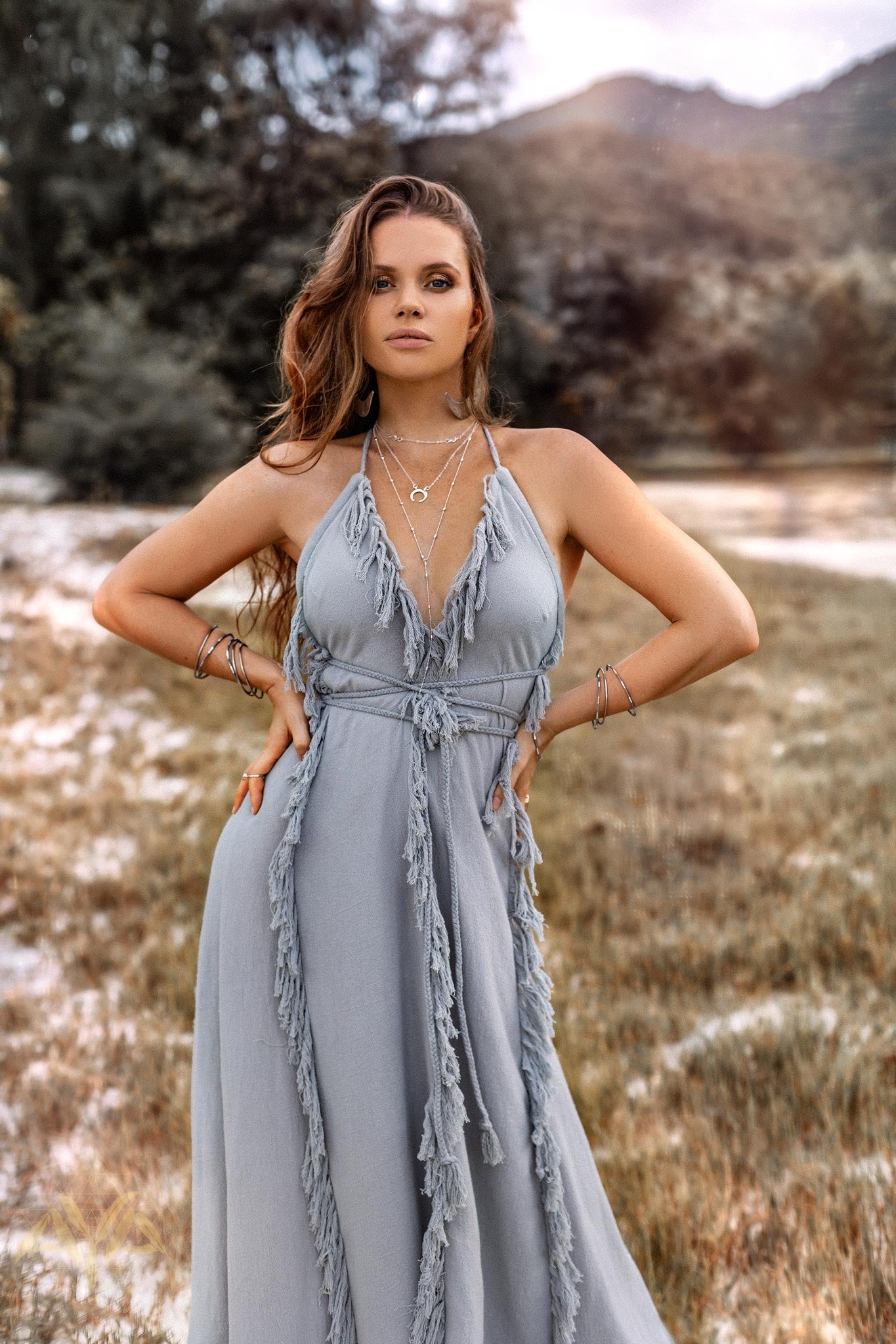 A model posing gracefully in a field, showcasing the deep halter V-neck and structured braided belt of the Sky Blue goddess dress.